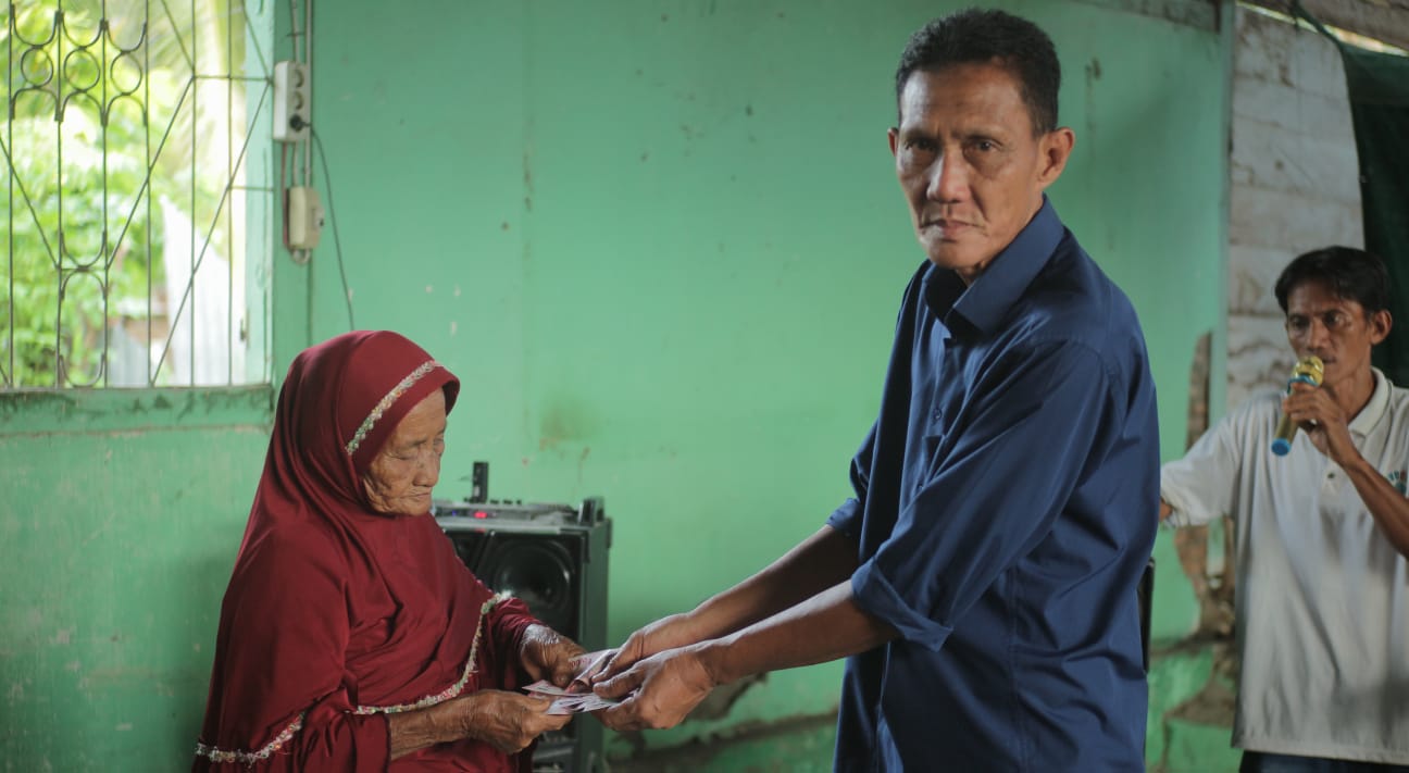 Kades Palasa Tengah, Abdul Rauf saat menyerahkan BLT-DD kepada salah satu KPM di Kantor Desa Palasa Tengah, Jumat (19/6/2026). Foto : HALOSulteng.com/DAL.